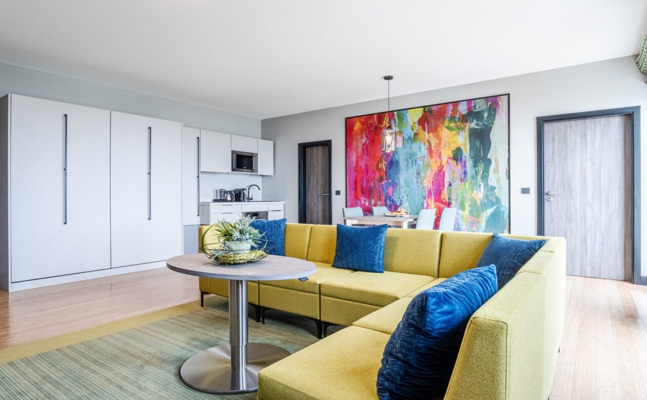 Modern eingerichtetes Zimmer im Das Ahlbeck Hotel & Spa mit großer Couch, Küchenzeile und farbenfrohem Wandbild