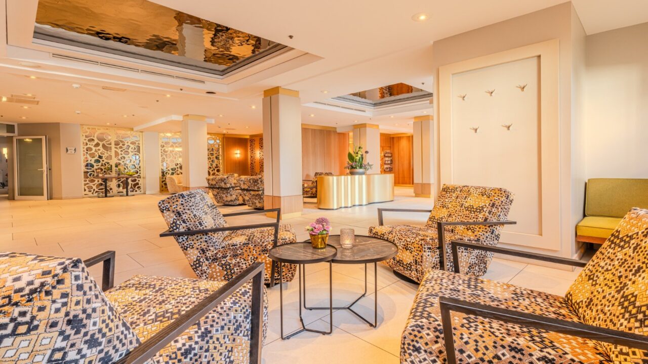 Hotellobby DAS AHLBECK HOTEL & SPA mit Schwingsesseln, Blumengesteck auf goldenem Sideboard als Dekoelement
